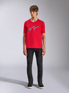 Alpinestars Ageless Shadow CSF Tee, Kurzarm-T-Shirt, Rot, vorderseitiges Ageless-Logo mit weißen und schwarzen Umrissen, getragen von einem Modell mit schwarzer Hose und Sneakern, lässige Motorsport-Streetwear