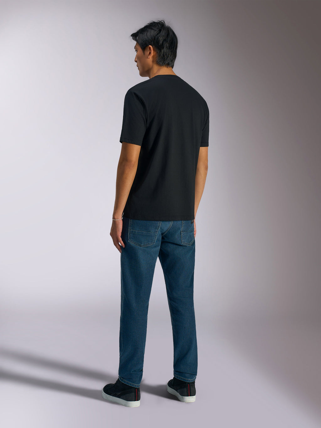 Alpinestars Ageless Shadow CSF T-Shirt, Kurzarm-T-Shirt, Schwarz, Rückansicht, kombiniert mit blauen Jeans und schwarzen Sneakern, lässige, vom Motorsport inspirierte Streetwear