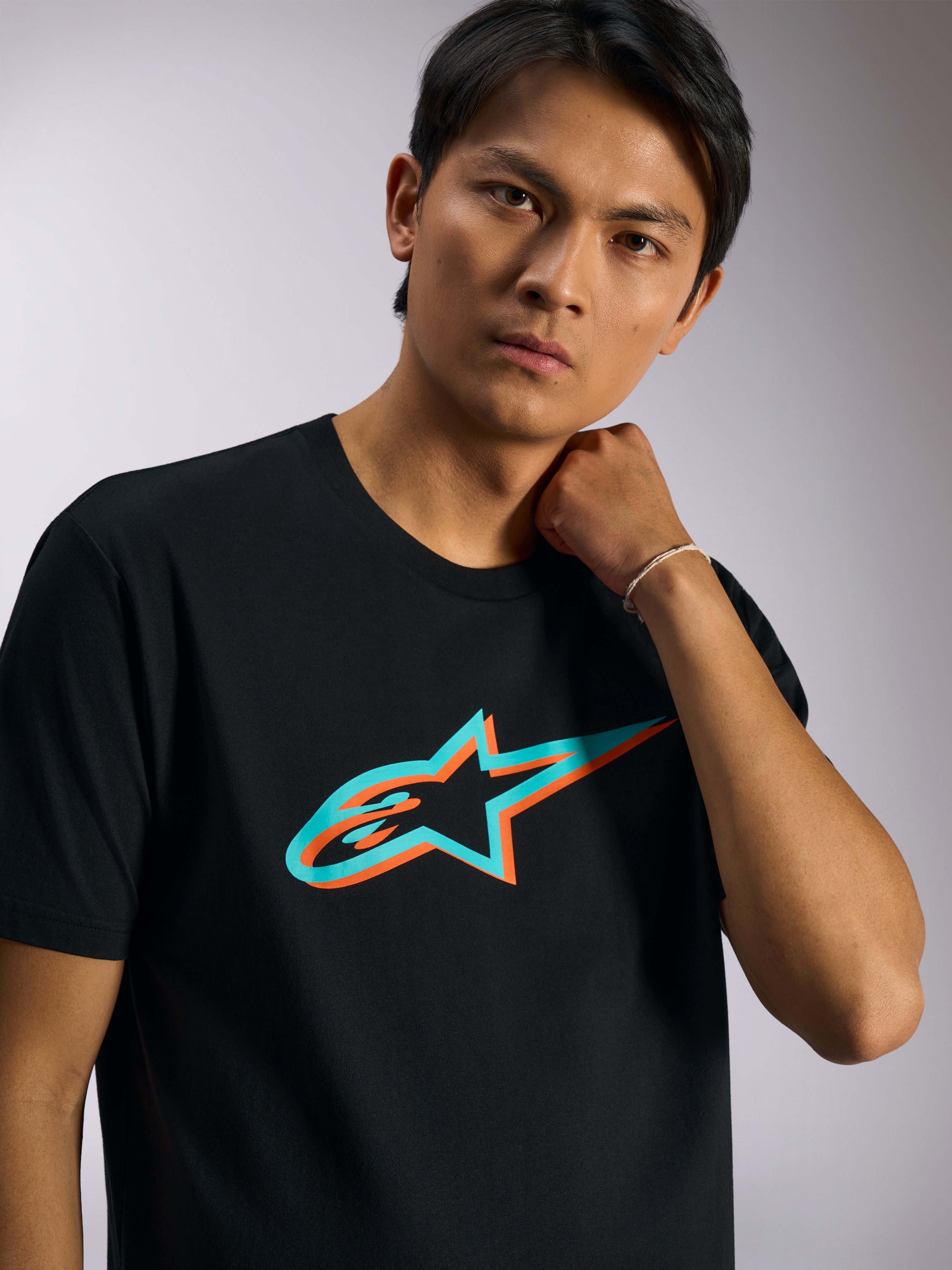 Alpinestars Ageless Shadow CSF Tee, Kurzarm-T-Shirt, Schwarz mit türkisfarbenem und orangefarbenem Schatten-Logo, am Model, lässige vom Motorsport inspirierte Streetwear