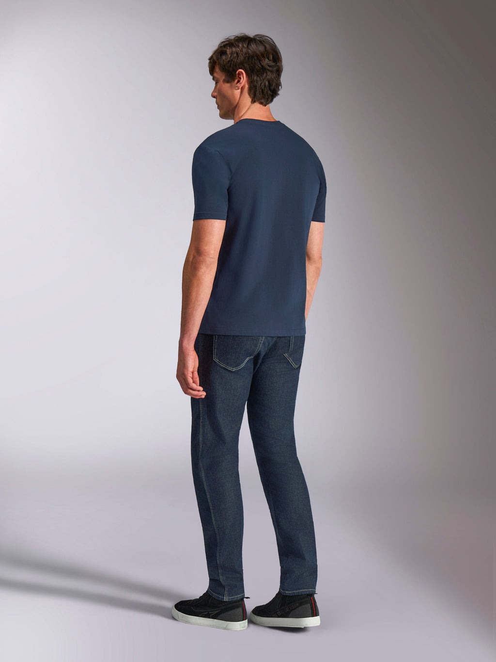 Alpinestars Ageless Shadow CSF Tee, kurzärmeliges T-Shirt, Marineblau, Rückansicht am Modell, getragen mit dunklen Denim-Jeans und schwarzen Sneakern, lässige Lifestyle-Streetwear