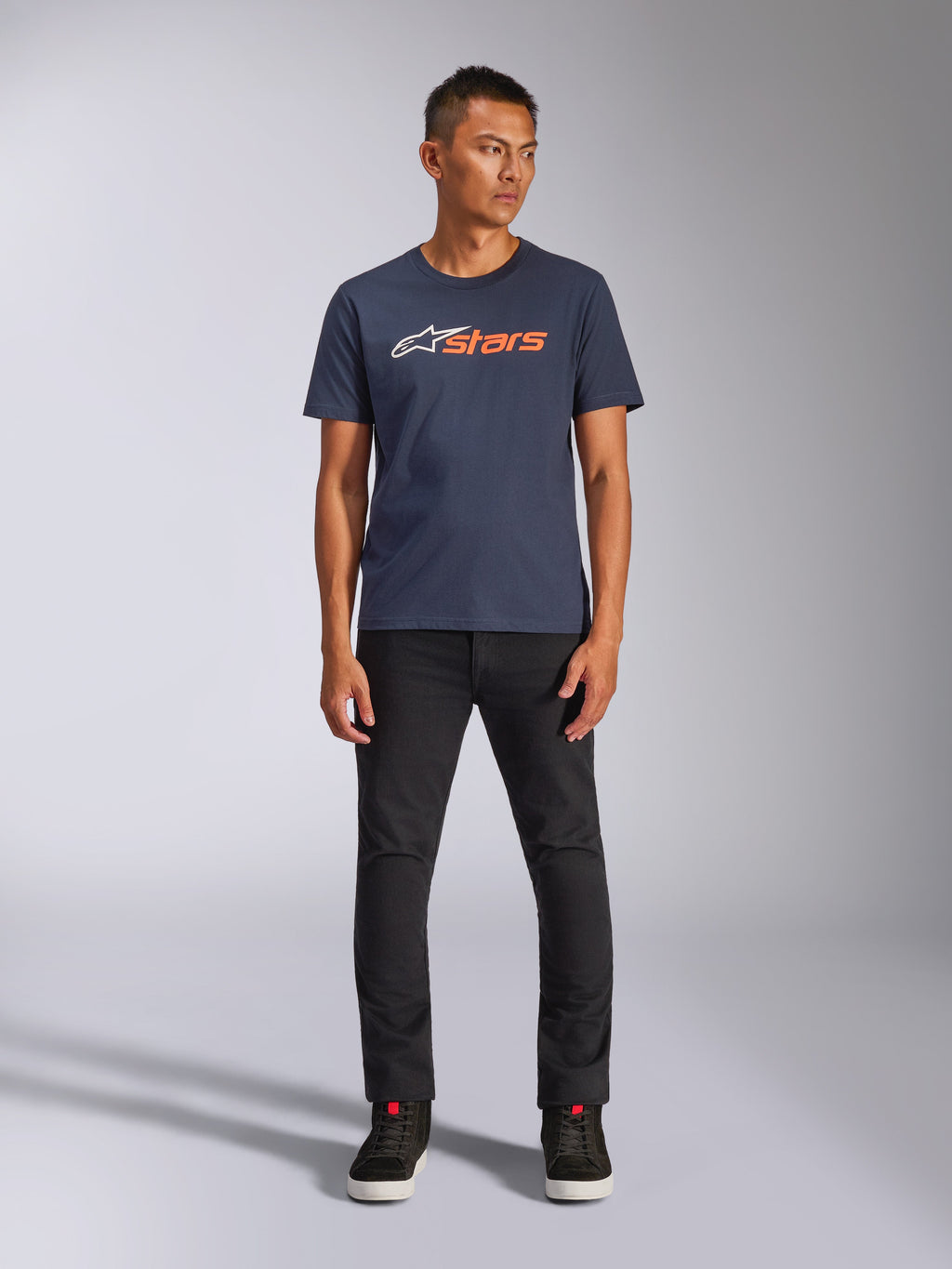 Alpinestars Blaze 2.0 CSF Tee, kurzärmeliges T-Shirt, Marineblau mit weißem und orangefarbenem Astars-Logo, getragen mit schwarzer Hose und schwarzen Sneakern, lässige, vom Motorsport inspirierte Streetwear