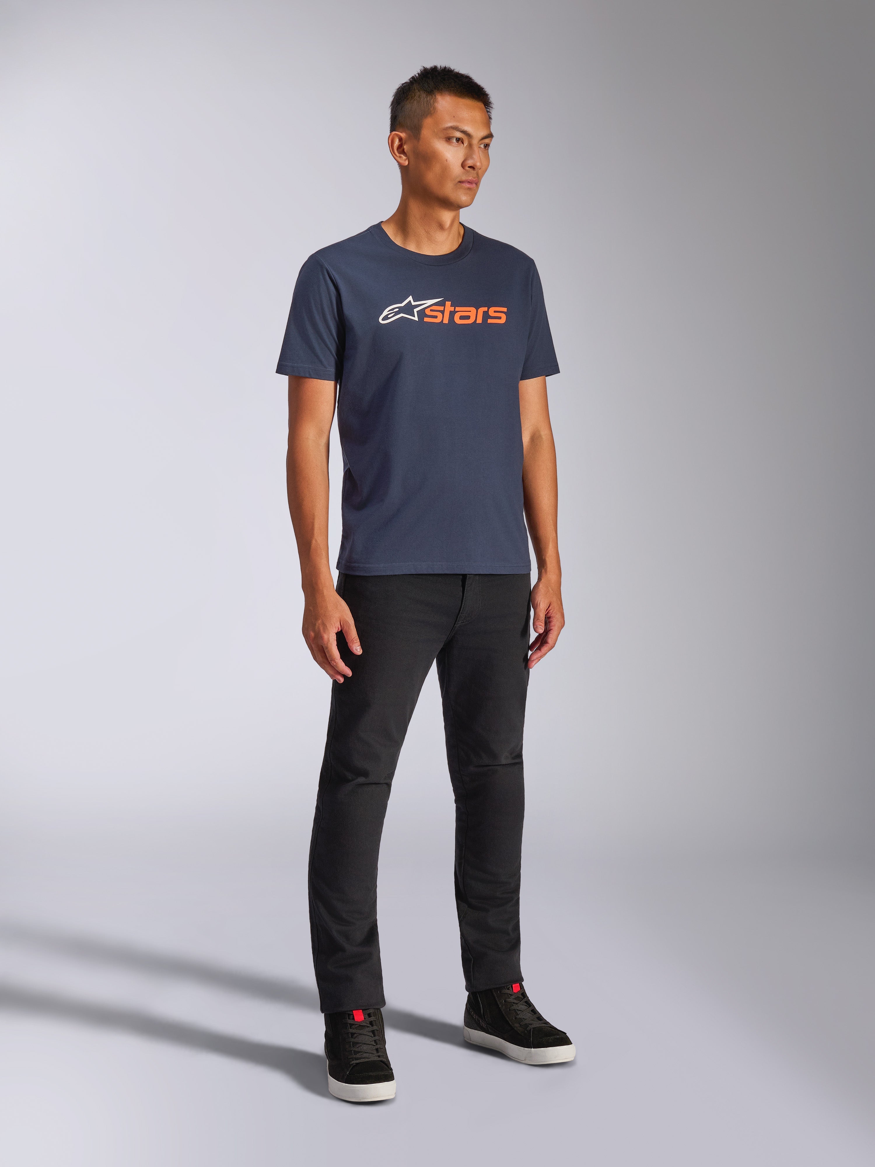 Alpinestars Blaze 2.0 CSF Tee, Kurzarm-T-Shirt, Navyblau mit weißem und orangefarbenem Blaze-Logo, getragen von einem Model mit schwarzer Hose und Sneakern, lässige, vom Motorsport inspirierte Streetwear