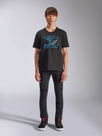 Alpinestars CSF Tee, Kurzarm-T-Shirt, Schwarz, blaue Motocross-Helm-Grafik mit weißem Logo, getragen von einem Model mit schwarzer Hose und schwarzen Sneakern, lässige Motorsport-inspirierte Streetwear