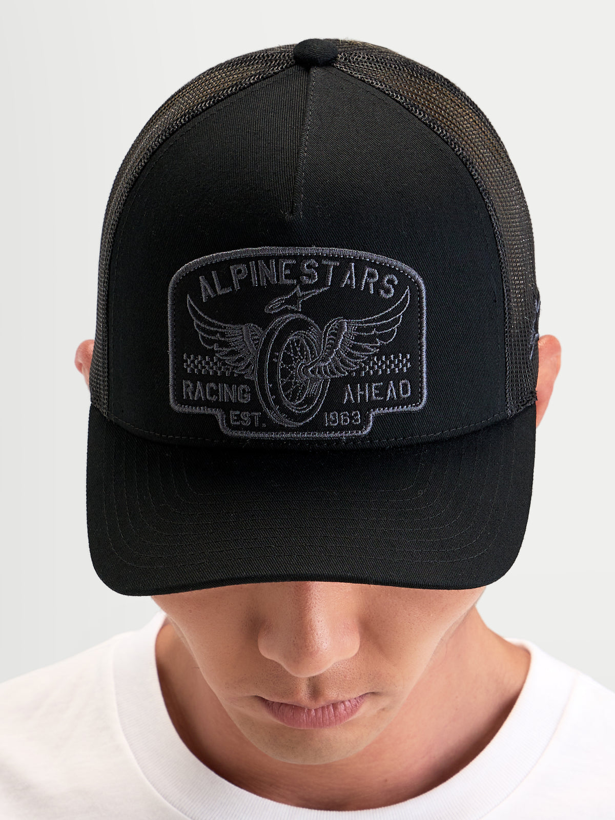 Alpinestars Heritage Patch Trucker-Kappe, schwarze Sportswear-Kappe mit gebogenem Schirm, strukturierter Krone und großem gestickten Logo-Patch, getragen von einer Person