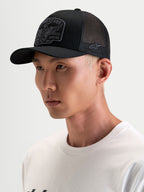 Alpinestars Heritage Patch Trucker-Kappe, schwarze und graue Trucker-Mütze mit gebogenem Schirm, strukturierter Krone und gesticktem Front-Logo-Patch, getragen von einem Model