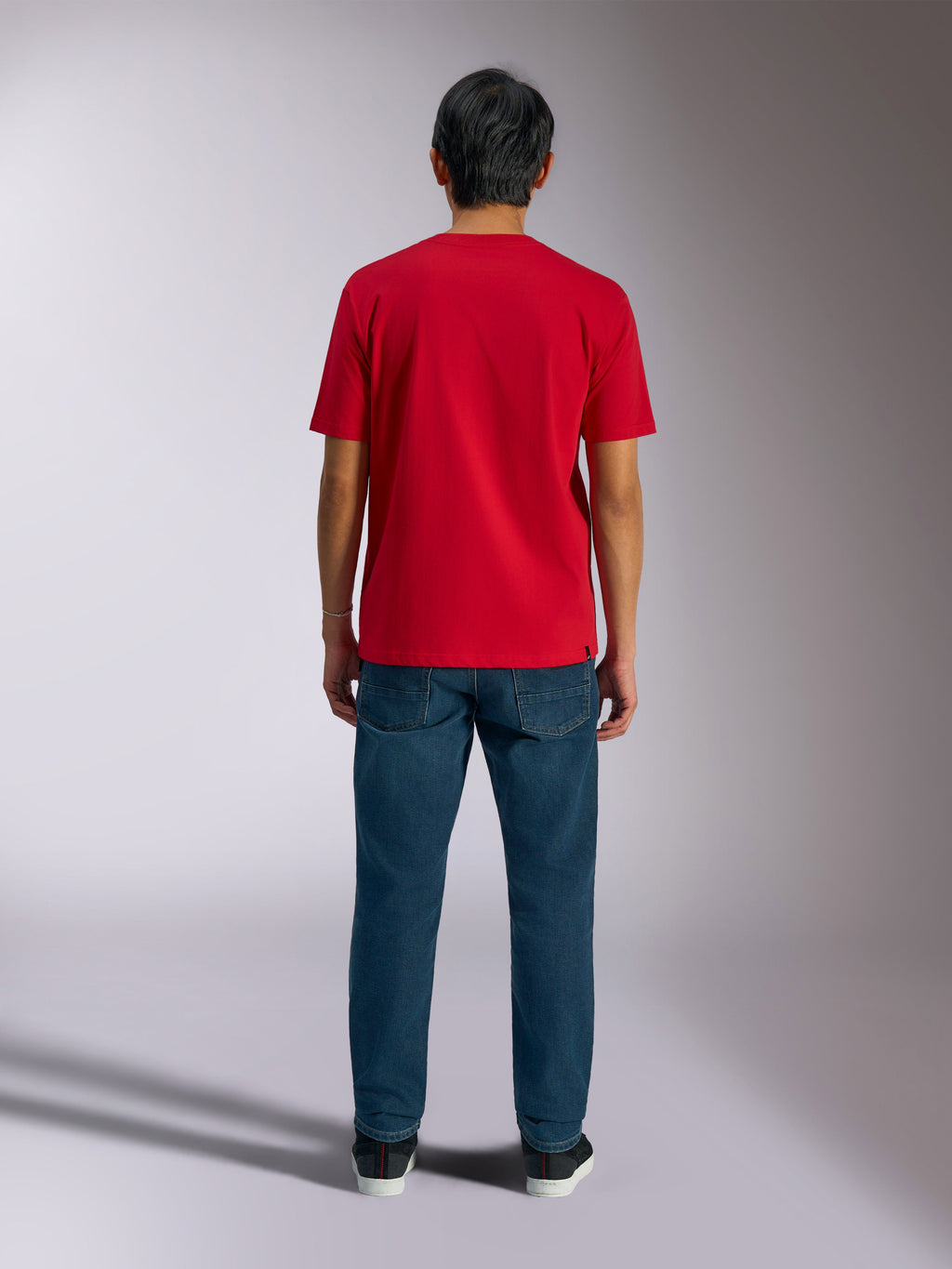Alpinestars Ageless Shadow CSF T-Shirt, Rückansicht eines roten Kurzarm-T-Shirts, kombiniert mit dunkelblauen Denim-Jeans und schwarzen Sneakern, lässige Motorsport-Streetwear