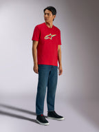 Alpinestars Ageless Shadow CSF Tee, Kurzarm-T-Shirt, Rot, mit Ageless Shadow-Logo sowie gelben und blauen Akzenten, getragen von einem Model mit Denim-Jeans und schwarzen Sneakern, lässige Motorsport-Streetwear
