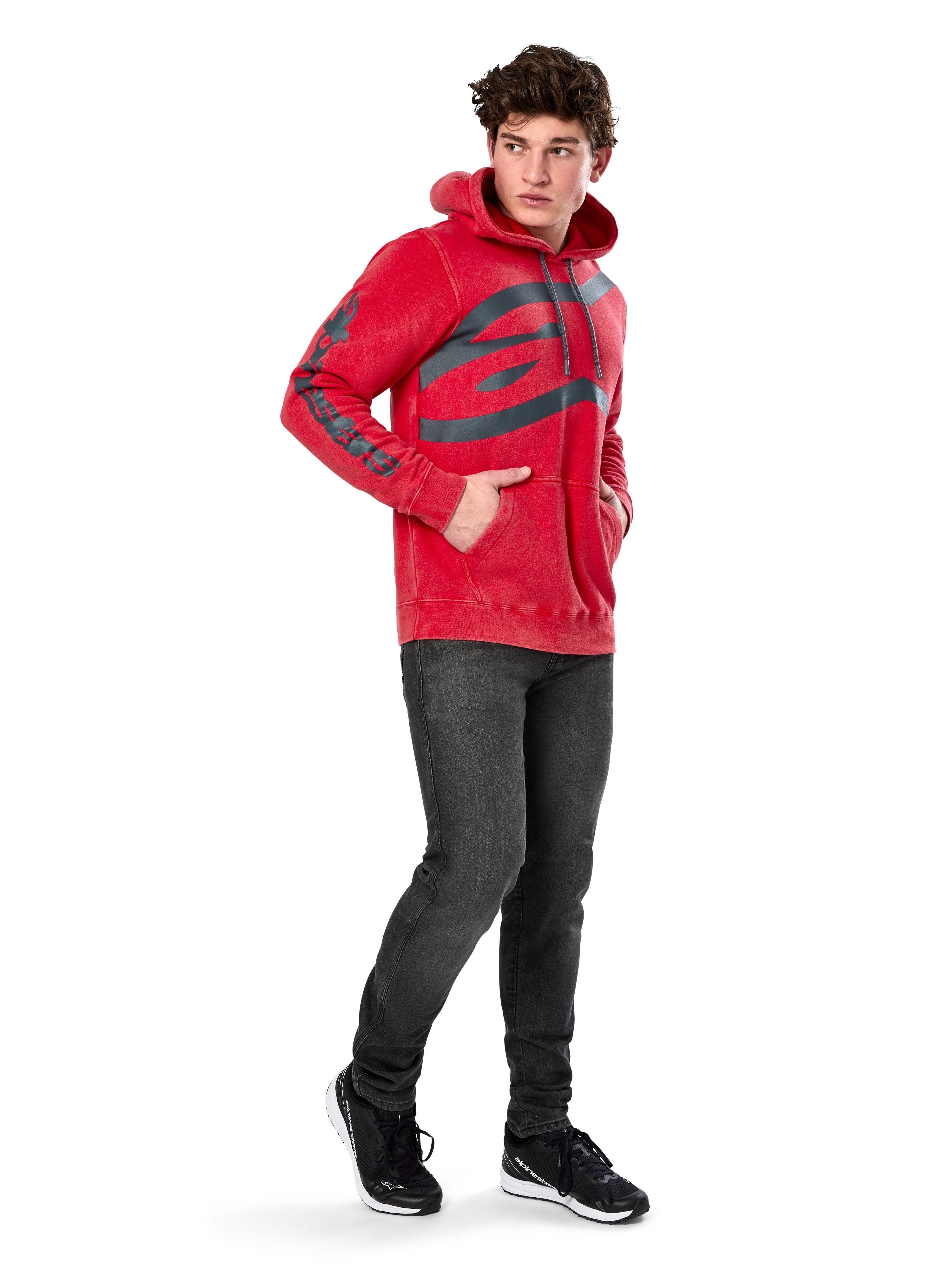 Alpinestars Unbound Hoodie, Red garment-dyed pullover fleece, extra-large dark logo on chest and wordmark on sleeves, kangaroo pocket, drawstring hood, worn by model with dark gray jeans and black sneakers, casual motorsport-inspired streetwear