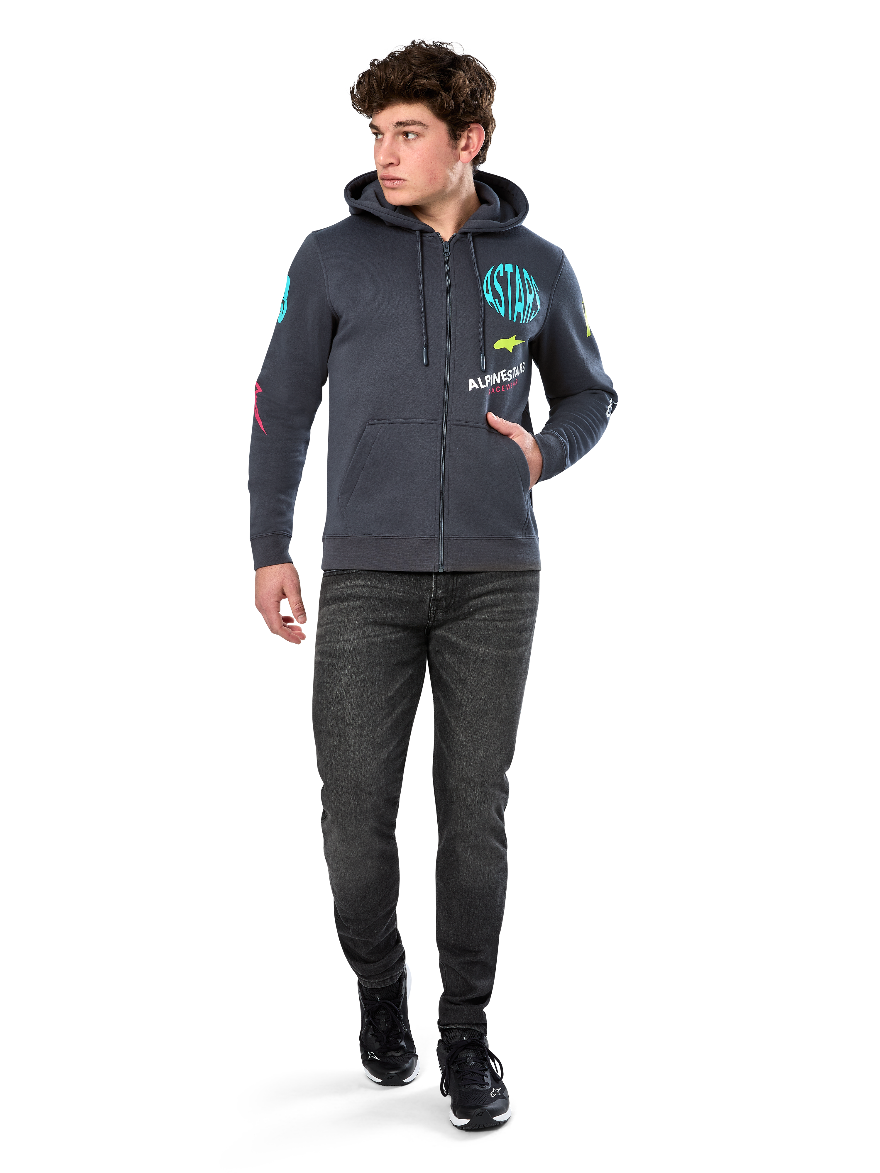 Alpinestars Variegate Hoodie, zip-front fleece hoodie, Gunmetal gray, worn by model with black jeans and sneakers, featuring teal 'ASTARS' branding and colorful logo art on sleeves and chest, casual motorsport-inspired streetwear