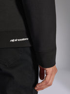 Alpinestars Positive Crew, schwarzes Pullover-Sweatshirt, Detailaufnahme von geripptem Saum und Ärmelbündchen mit weißem Alpinestars-Logo, hochwertige Stofftextur, lässige vom Motorsport inspirierte Sportbekleidung