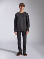Alpinestars Positive Crew Sweatshirt, lässiger schwarzer Crewneck, kleines weißes Logo auf der Brust, V-Stitch-Ausschnitt, Ganzkörper-Studioaufnahme mit Model in schwarzer Hose und Sneakern, Motorsport-inspirierte Lifestyle-Bekleidung