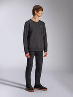 Alpinestars Positive Crew, Pullover-Sweatshirt, Schwarz, kleines weißes Alpinestars-Logo auf der Brust, gerippter Kragen mit V-Detail, Rippbündchen an Ärmeln und Saum, getragen von einem Model mit schwarzer Hose und Sneakern, lässige vom Motorsport inspirierte Streetwear
