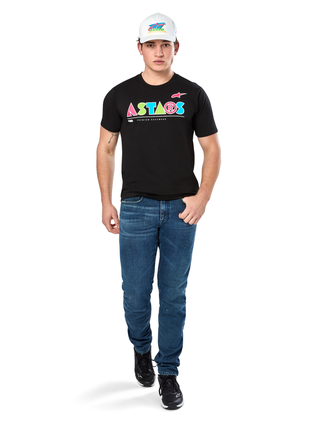 Male model wearing Alpinestars Cereal CSF Tee, Black Short Sleeve T-Shirt with colorful geometric ASTARS logo, paired with blue jeans and white cap, casual motorsport-inspired streetwear.