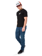 Alpinestars Formulate Csf Tee, Kurzarm-T-Shirt, Schwarz mit weißem Astars-Logo auf der Brust, getragen von einem Model mit blauen Jeans, einer bordeauxroten und weißen Kappe und schwarzen Sneakern, lässige, vom Motorsport inspirierte Streetwear