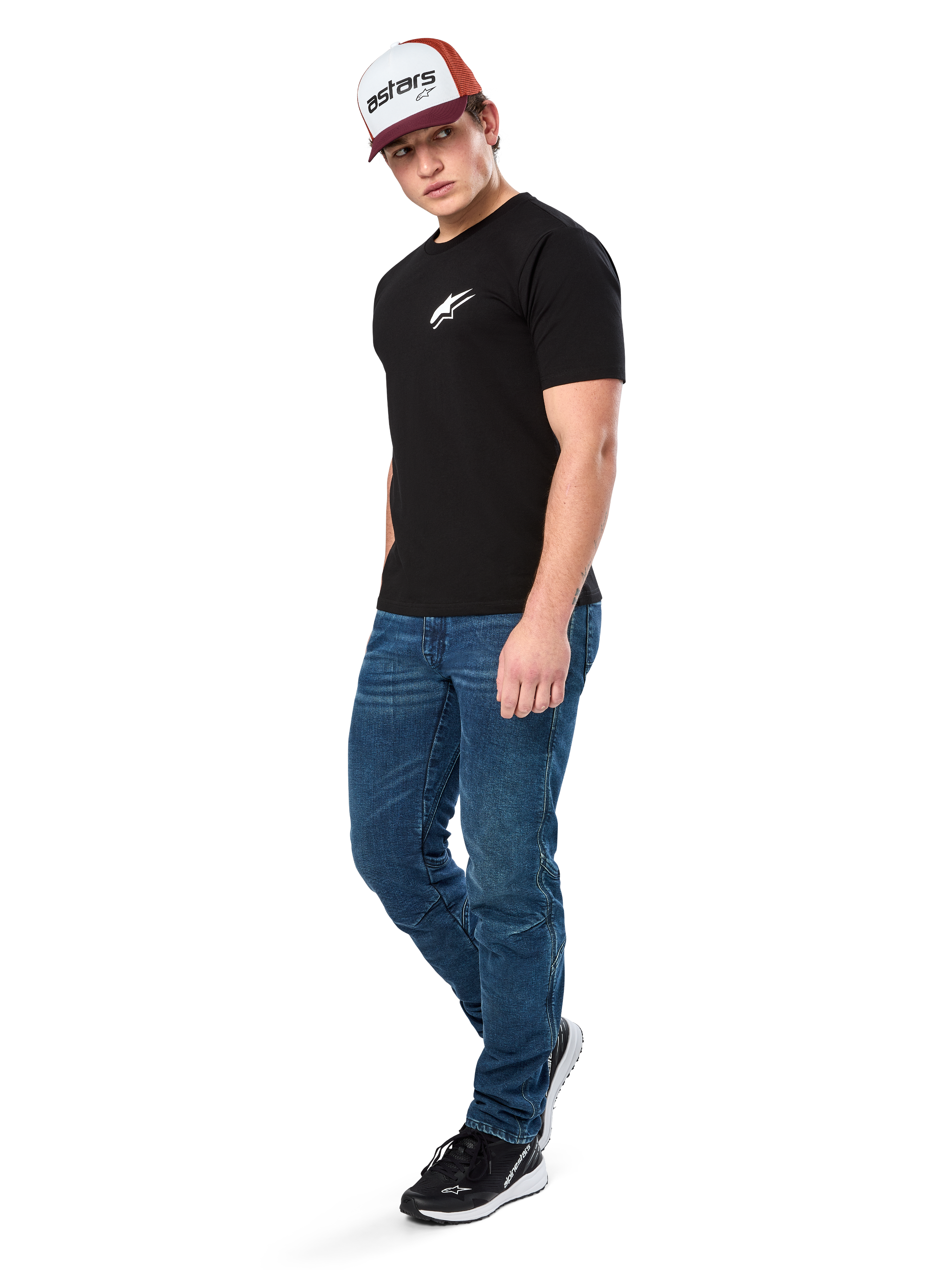 Alpinestars Formulate Csf Tee, Kurzarm-T-Shirt, Schwarz mit weißem Astars-Logo auf der Brust, getragen von einem Model mit blauen Jeans, einer bordeauxroten und weißen Kappe und schwarzen Sneakern, lässige, vom Motorsport inspirierte Streetwear