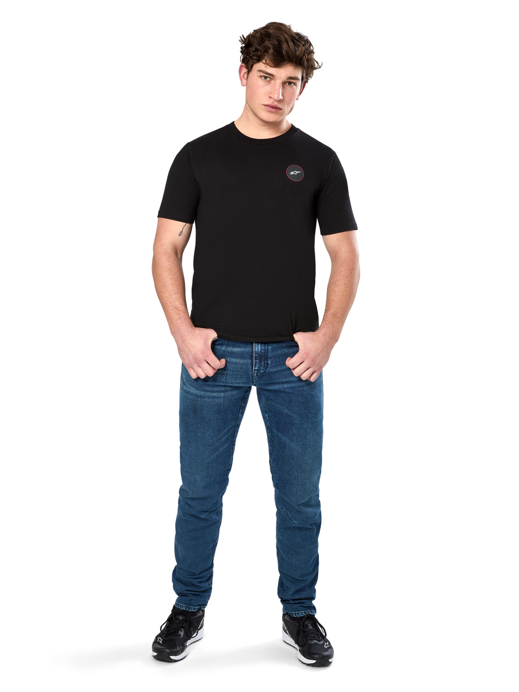 Alpinestars Dot Carbon CSF Tee, Kurzarm-T-Shirt, Schwarz, kleines kreisförmiges Astars Dot-Logo auf der Brust, getragen mit blauen Jeans und schwarzen Sneakern, lässige Motorsport-Streetwear