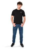 Alpinestars Dot Carbon CSF Tee, Kurzarm-T-Shirt, Schwarz, kleines kreisförmiges Astars Dot-Logo auf der Brust, getragen mit blauen Jeans und schwarzen Sneakern, lässige Motorsport-Streetwear