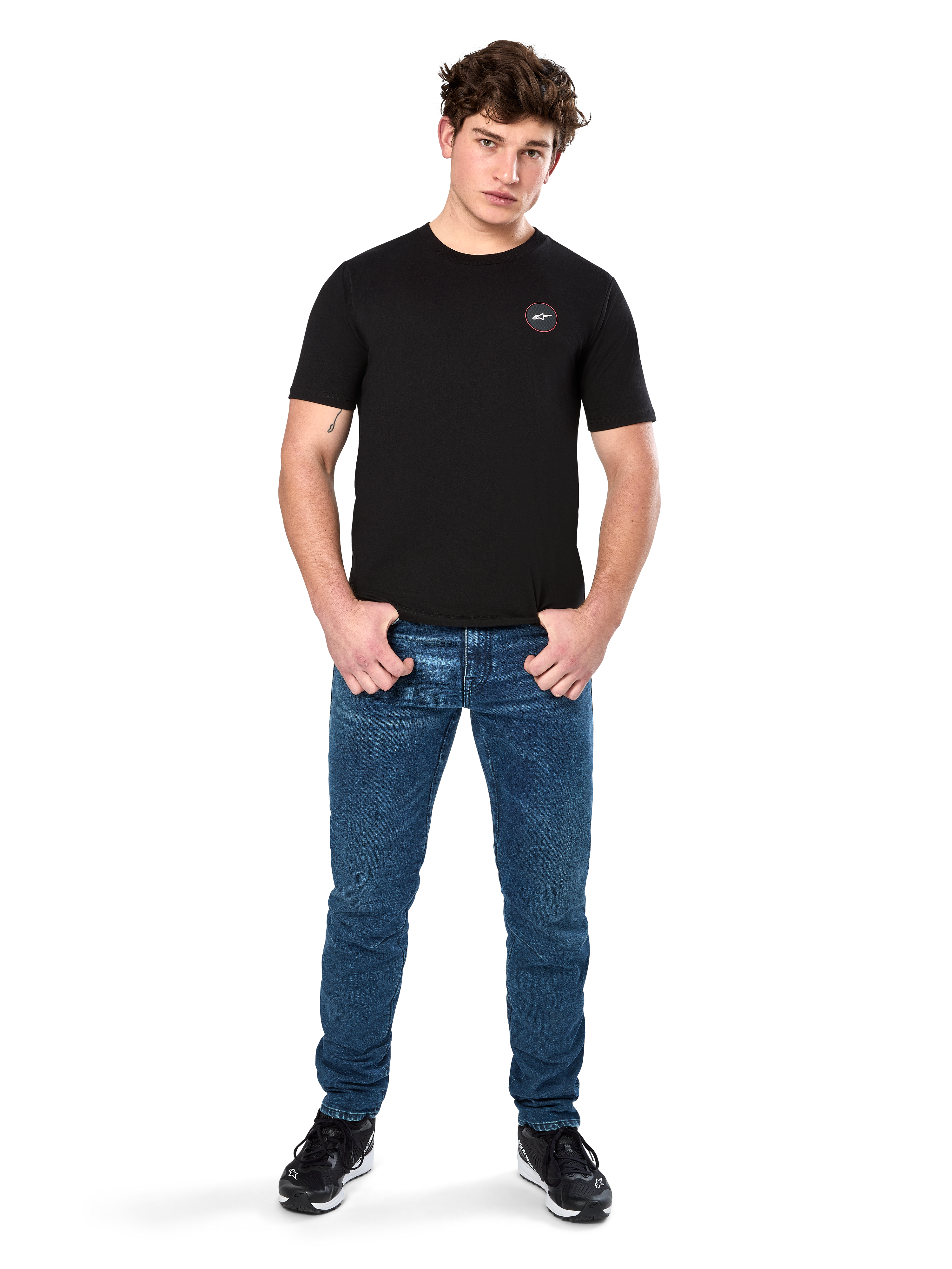 Alpinestars Dot Carbon CSF Tee, Kurzarm-T-Shirt, Schwarz, kleines kreisförmiges Astars Dot-Logo auf der Brust, getragen mit blauen Jeans und schwarzen Sneakern, lässige Motorsport-Streetwear