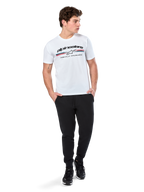 Alpinestars Prevail CSF Tee, Kurzarm-T-Shirt, Weiß, mit dreifarbigem Streifenlogo im Paddock-Stil und Alpinestars-Branding auf der Vorderseite, getragen von einem Model mit schwarzen Jogginghosen und schwarzen Sneakern, lässige Motorsport-Streetwear
