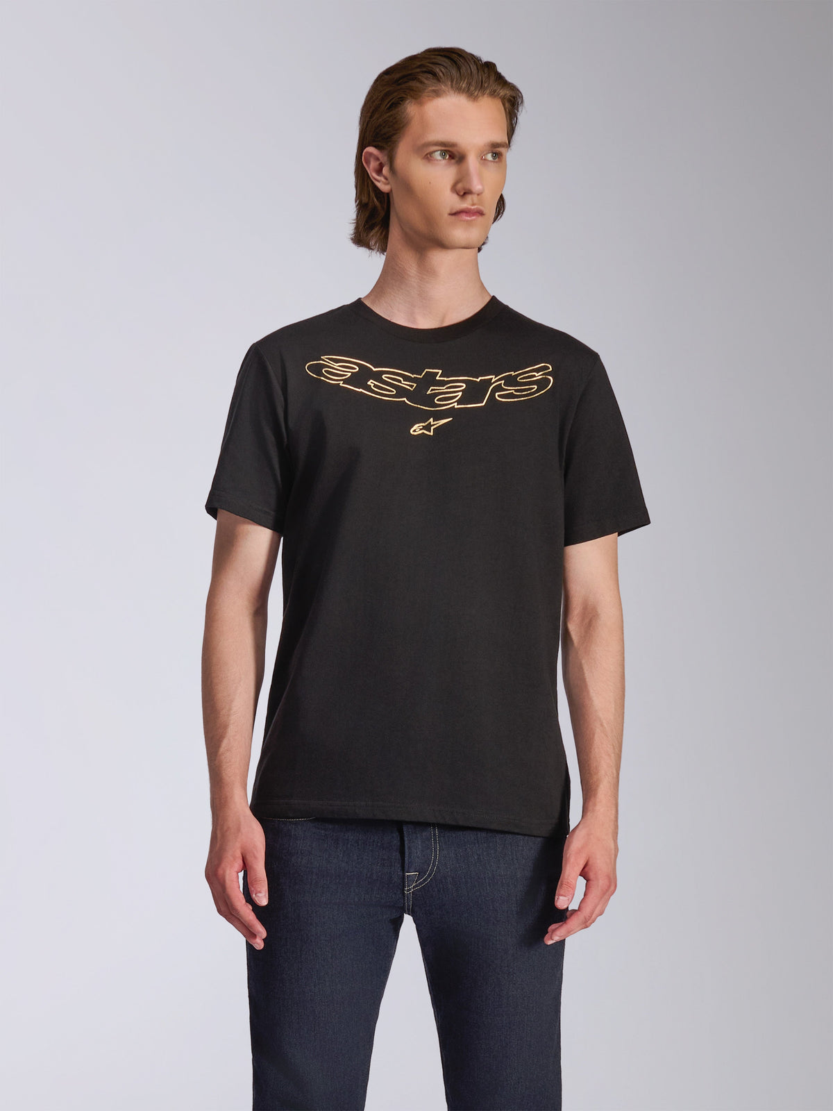 Alpinestars Luxo CSF Tee, Kurzarm-T-Shirt, Schwarz, gold umrandetes Astars-Logo auf der Brust, getragen mit dunkelblauen Jeans, lässige Motorsport-Streetwear
