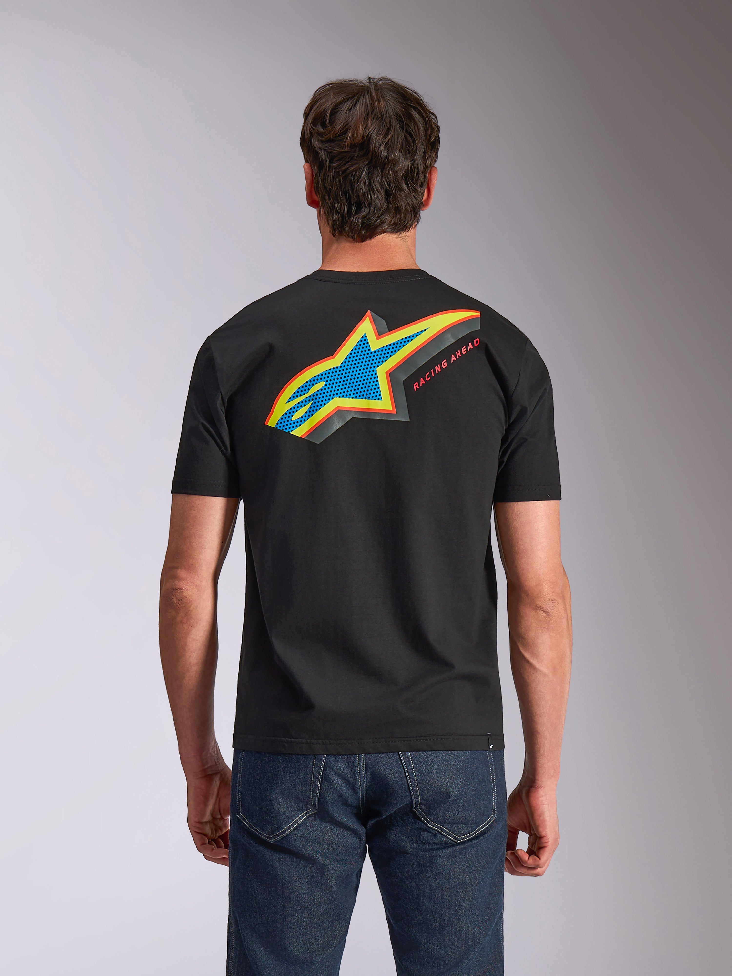 Alpinestars Angler CSF Tee, kurzärmeliges T-Shirt, Schwarz, Rückansicht mit lebendigem mehrfarbigem Astars-Logo mit perforierter Füllung und „RACING AHEAD“-Schriftzug, getragen mit blauen Jeans, lässige Motorsport-inspirierte Bekleidung.