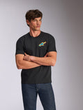 Alpinestars Angler CSF Tee, kurzärmeliges T-Shirt, Schwarz, mit einem lebendigen, mehrfarbigen Astars-Logo auf der Brust, getragen von einem Model mit verschränkten Armen und blauen Jeans, lässige, vom Motorsport inspirierte Streetwear