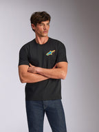 Alpinestars Angler CSF Tee, kurzärmeliges T-Shirt, Schwarz, mit einem lebendigen, mehrfarbigen Astars-Logo auf der Brust, getragen von einem Model mit verschränkten Armen und blauen Jeans, lässige, vom Motorsport inspirierte Streetwear