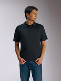 Alpinestars Impetus Sport Polo, schwarzes Kurzarm-Poloshirt, Drei-Knopf-Leiste und Selbstkragen, kleines graues Astars-Logo auf der linken Brust, getragen mit blauen Jeans, lässige, vom Motorsport inspirierte Sportbekleidung