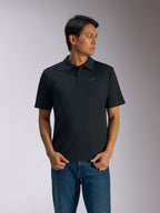 Alpinestars Impetus Sport Polo, schwarzes Kurzarm-Poloshirt, Drei-Knopf-Leiste und Selbstkragen, kleines graues Astars-Logo auf der linken Brust, getragen mit blauen Jeans, lässige, vom Motorsport inspirierte Sportbekleidung