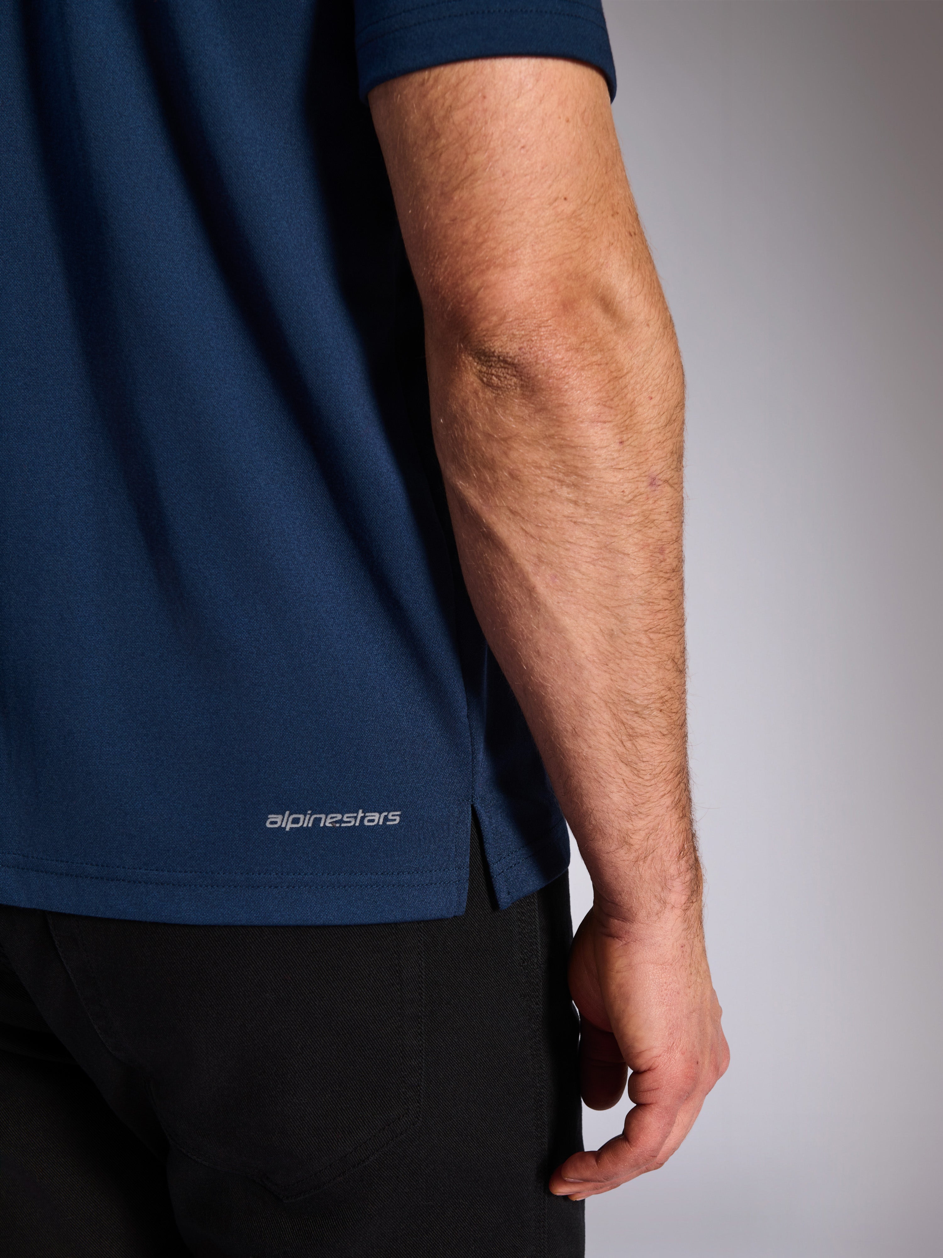Alpinestars Impetus Sport Polo, Navy, Nahaufnahme des unteren Saums mit Alpinestars-Schriftzug und Seitenschlitz, Mock-Mesh-Strickstruktur, lässige Motorsport-Sportbekleidung