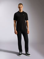 Alpinestars Endeavor Classic Polo, kurzärmeliges Piqué-Poloshirt, Schwarz, kleines weißes Astars-Logo auf der Brust, Rippkragen und Ärmelbündchen, getragen von einem Model mit schwarzer Hose und Sneakern, lässige Motorsport-Streetwear