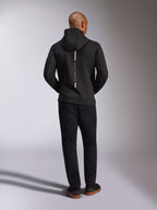 Alpinestars Insight Kapuzenpullover, Schwarz, Rückansicht am Modell, mit einem vertikalen weißen Streifen-Logo auf dem Rücken und dem Schriftzug „Racing Ahead“, legerer Sportswear-Hoodie aus Tri-Blend-Doppelvlies, kombiniert mit einer schwarzen Hose.