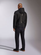 Alpinestars Insight Hoodie, schwarzer Sport-Kapuzenpullover, Rückansicht mit vertikalem weißem Streifen und „RACING AHEAD“-Schriftzug, Ärmellogo, kombiniert mit schwarzer Hose und Sneakern, lässiges, vom Motorsport inspiriertes Design