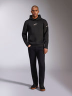 Alpinestars Insight Hoodie, schwarzer Kapuzenpullover mit weißem Astars-Logo auf der Brust und am Ärmel, getragen von einem Model mit schwarzer Hose und schwarzen Sneakern, lässige, vom Motorsport inspirierte Streetwear