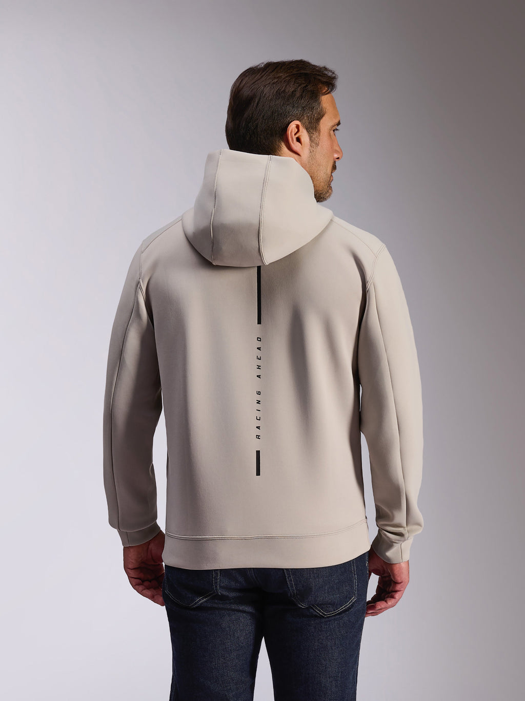 Alpinestars Insight Hoodie in Cement, Rückansicht eines Models in einem hellgrauen Kapuzensweatshirt, schwarzes vertikales Streifen-Logo mit 'RACING AHEAD' Text, lässiger vom Motorsport inspirierter Doppel-Fleece-Hoodie.