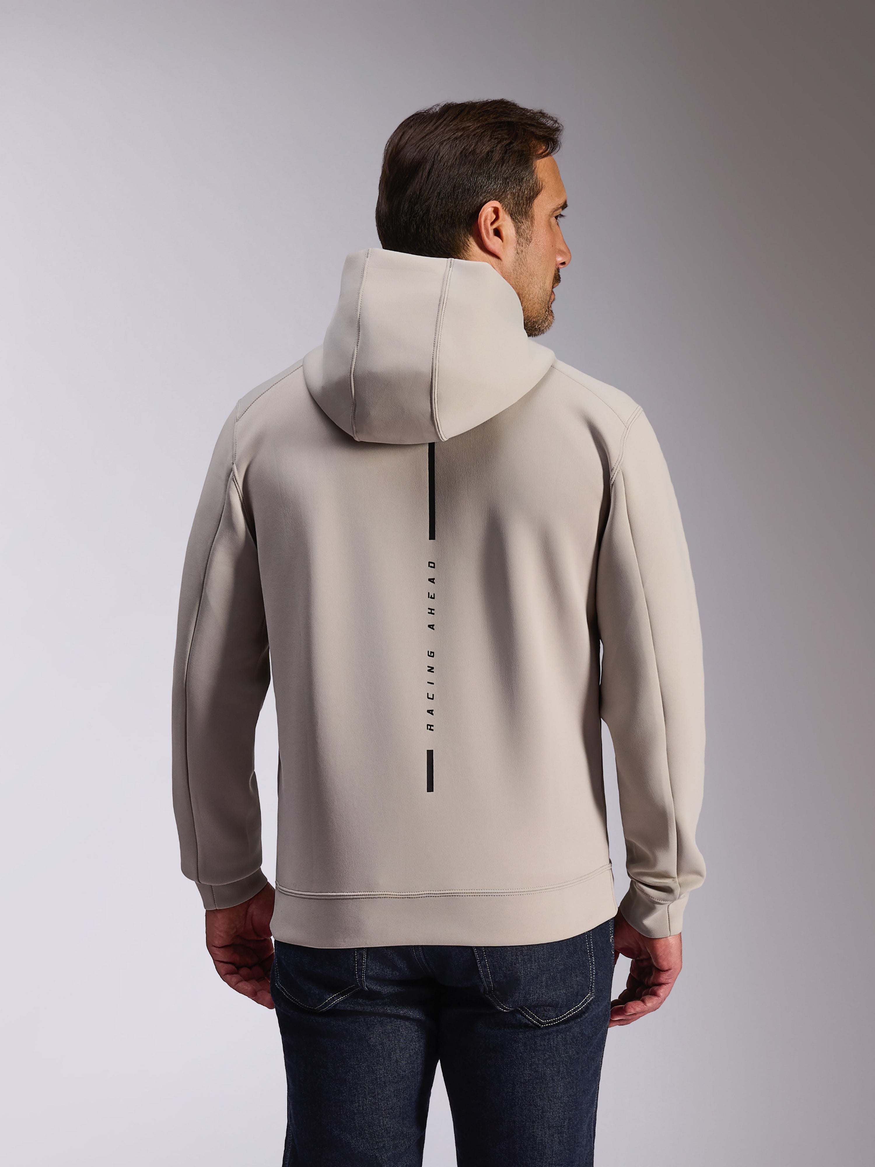 Alpinestars Insight Hoodie in Cement, Rückansicht eines Models in einem hellgrauen Kapuzensweatshirt, schwarzes vertikales Streifen-Logo mit 'RACING AHEAD' Text, lässiger vom Motorsport inspirierter Doppel-Fleece-Hoodie.