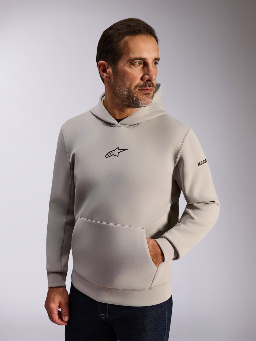 Alpinestars Insight Kapuzenpullover, lässige Lifestyle-Streetwear, zementgraues Fleece, schwarzes Astars-Logo auf der Vorderseite, Kängurutasche, Wortmarke am Ärmel, Kapuze mit Mesh-Futter, moderne vom Motorsport inspirierte Bekleidung
