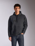 Alpinestars Emergent Oversized Hoodie, Schwarz, männliches Model trägt einen Oversized-Fleece-Kapuzenpullover, tonales 3D-gesticktes Astars-Logo, Kängurutasche, Kapuze mit Kordelzug, lässige vom Motorsport inspirierte Streetwear