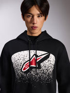 Alpinestars Obsessed Hoodie, schwarzer Fleece-Kapuzenpullover, mit einem rot-weißen Astars-Logo in einer weiß gepunkteten MX-Verlaufsgrafik auf der Brust, von einem Model getragen, lässige Motorsport-Streetwear mit verstellbarem Kordelzug an der Kapuze