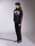 Alpinestars Obsessed Hoodie, schwarzer Kapuzenpullover aus Fleece, mit einer großen weiß gesprenkelten Grafik auf der Brust, rotem Astars-Logo und rotem Branding an den Ärmeln, getragen von einem Model mit schwarzer Hose und Sneakern, lässige Motorsport-Streetwear