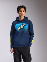 Alpinestars Obsessed Hoodie in Navy, worn by a male model, featuring a lime green Astars logo with bright blue MX gradation on the chest and yellow wordmark logos on the sleeves, casual motorsport-inspired streetwear.
