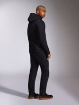 Alpinestars Ellipsoid Hoodie, schwarze Freizeit-Streetwear, Rückansicht an einem männlichen Model, Fleece-Kapuzenpullover mit Rippbündchen und Saum, getragen mit schwarzer Hose und Sneakern, modernes, vom Motorsport inspiriertes Design