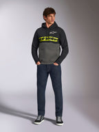Alpinestars Parallel Hoodie, Color-Block-Kapuzenpullover in Schwarz und Gunmetal-Grau, leuchtend gelbes Alpinestars-Wortlogo und weißes Stern-Logo auf der Brust, getragen von einem männlichen Model mit dunkelblauer Jeans und schwarzen Sneakern, lässige Motorsport-Streetwear