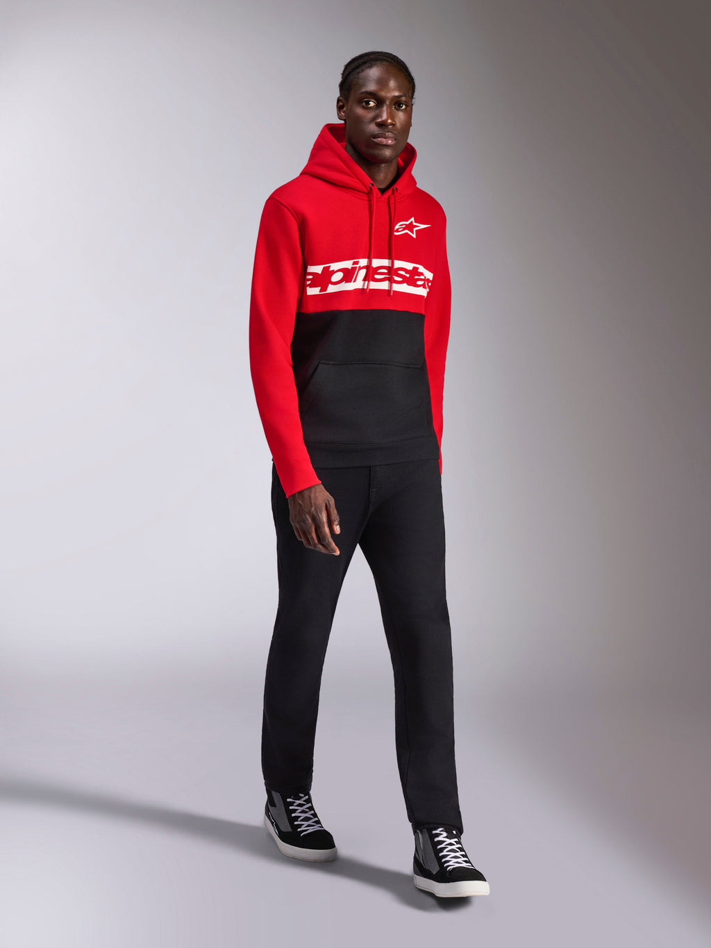 Alpinestars Parallel Hoodie, lässige Sportbekleidung, rot-schwarzes Color-Block-Design, weißer Alpinestars-Schriftzug und Stern-Logo auf der Brust, kombiniert mit schwarzer Hose und Sneakern, moderner, vom Motorsport inspirierter Look