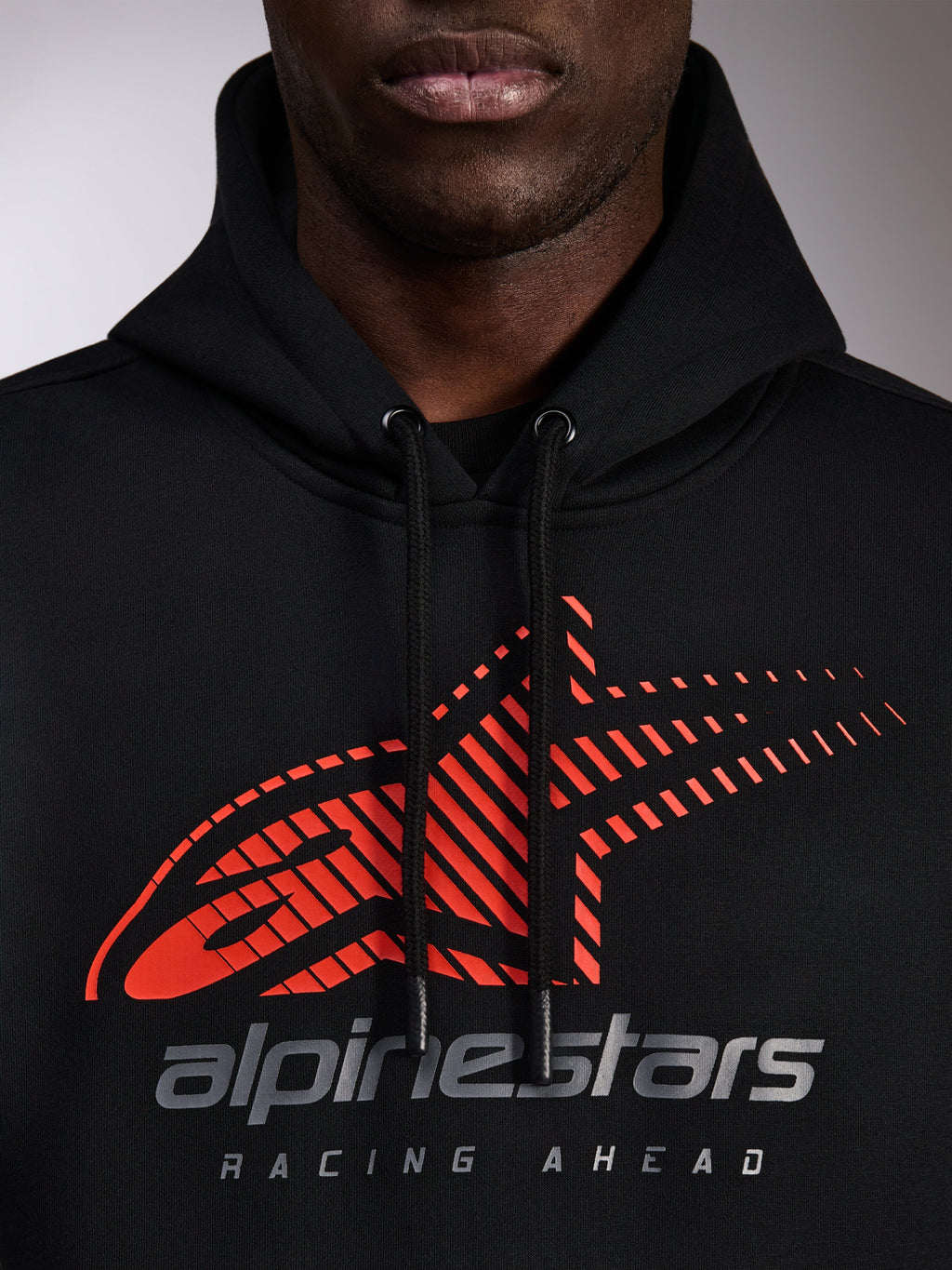 Alpinestars Pulse Hoodie, schwarzer Kapuzenpullover, Nahaufnahme der Brust mit rotem Astars-Logo mit Speed-Line-Fade und silbernem Branding, schwarze Kordelzüge mit Tauchspitzen, lässige Motorsport-Streetwear