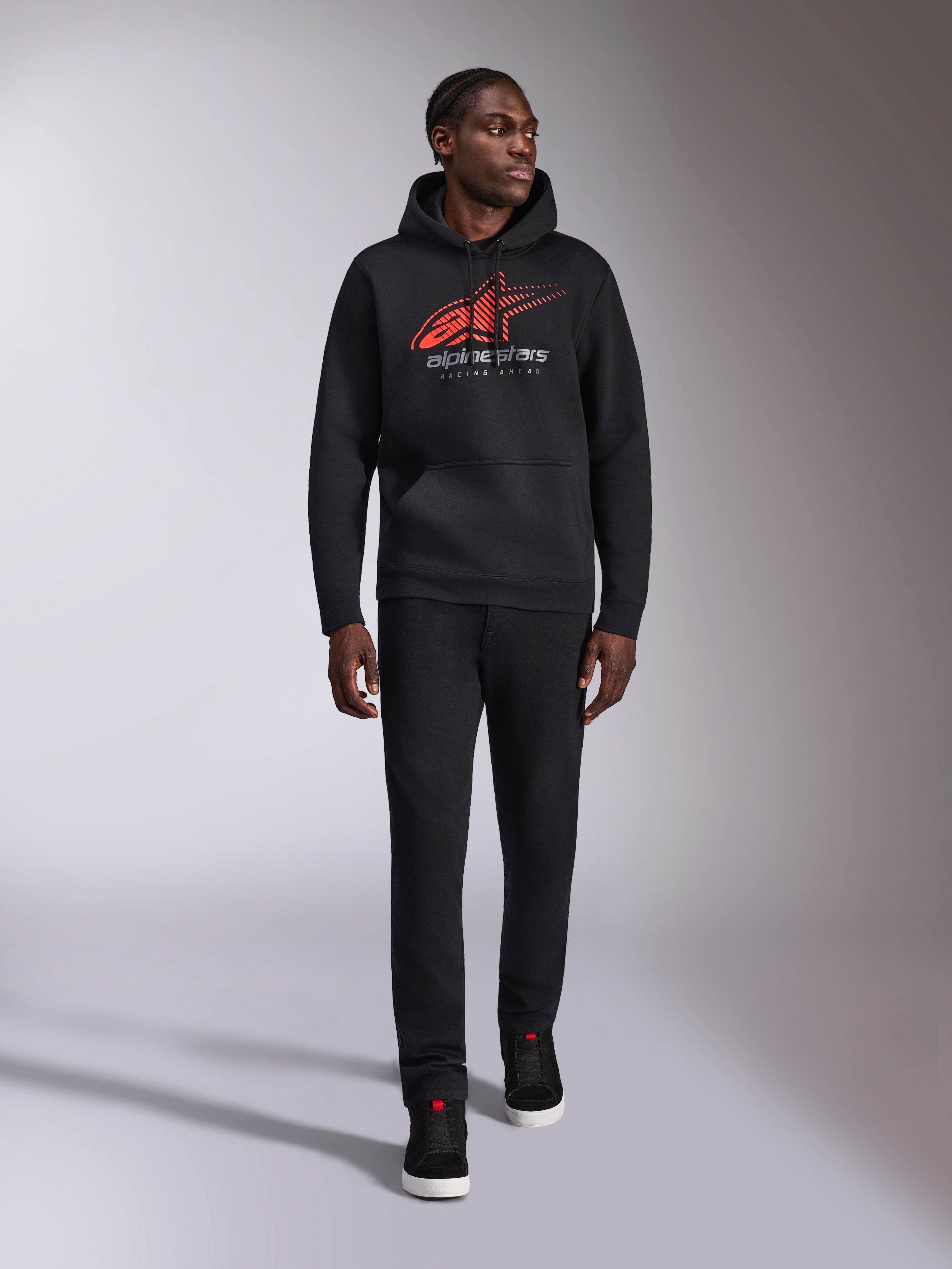 Alpinestars Pulse Hoodie, schwarzer lässiger Streetwear-Hoodie, rot-graues Astars-Logo mit Speed-Line-Verlauf auf der Brust, Kapuze mit Kordelzug, Kängurutasche vorne, lange Ärmel, kombiniert mit schwarzer Hose und Sneakern, vom Motorsport inspiriertes Design