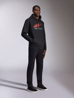 Alpinestars Pulse Hoodie, schwarzer Kapuzenpullover, mit rot-weißem Astars-Logo mit Speed-Line-Farbverlauf und „Racing Ahead“-Schriftzug, getragen mit passender schwarzer Hose und Sneakern, lässige, vom Motorsport inspirierte Streetwear.