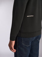 Alpinestars Cypher Hoodie, close-up view of the lower back and sleeve, Black double-face fleece with white Alpinestars word logo, worn with blue jeans, casual motorsport streetwear