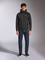 Model wearing the Alpinestars Cypher Hoodie, Black zip-front fleece hoodie, high-neck hood with a small white Astars logo on the chest, paired with dark denim jeans and black sneakers, casual motorsport-inspired streetwear