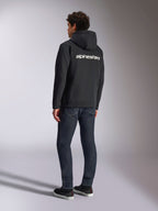 Alpinestars Transverse Hoodie, schwarzer Kapuzenfleece mit Reißverschluss, Rückansicht mit weißem Alpinestars-Schriftzug über den Schultern, kombiniert mit dunkelblauen Jeans und schwarzen Sneakern, lässige, vom Motorsport inspirierte Streetwear